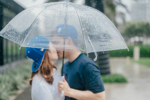 Romantic couple kisses under an umbrella during a rainy day, capturing a moment of love and protection.