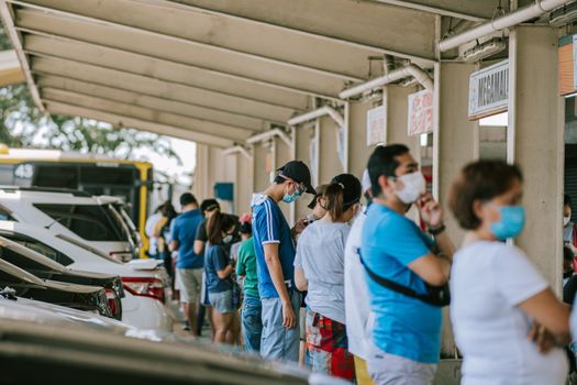 A group of people wearing face masks standing in line at an outdoor location.