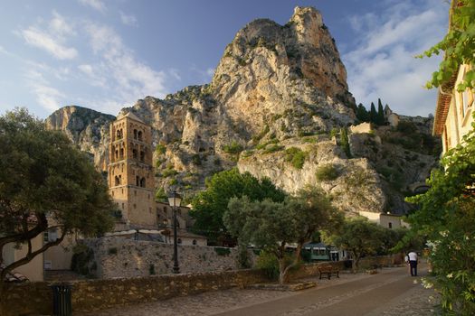 Charming village view with historic architecture and majestic cliffs at golden hour in Moustiers-Sainte-Marie, France.