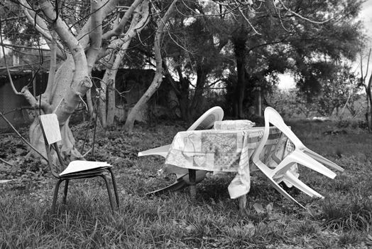 Black and white outdoor scene of overturned chairs and table in garden.