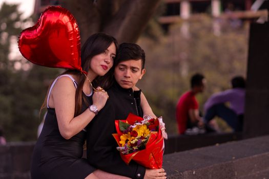 A couple sits close with a red heart-shaped balloon and a bouquet, capturing romance.