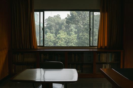 Serene library interior with table, chair, and window view of lush green trees.