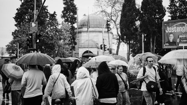 People in Istanbul crossing the street with umbrellas on a rainy day.
