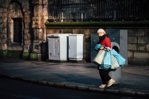 A woman in winter attire carries grocery bags on a Dublin street in morning light.
