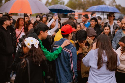 A diverse crowd gathers in the rain with umbrellas, conveying unity and emotion.