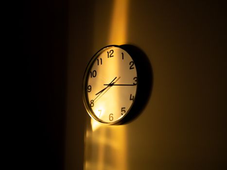 A wall clock illuminated by warm sunlight casts dramatic shadows, creating a contemplative mood.