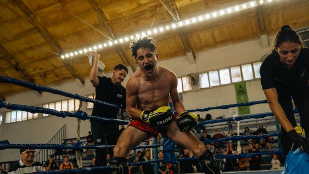 A victorious young boxer celebrates in the ring surrounded by cheering supporters.