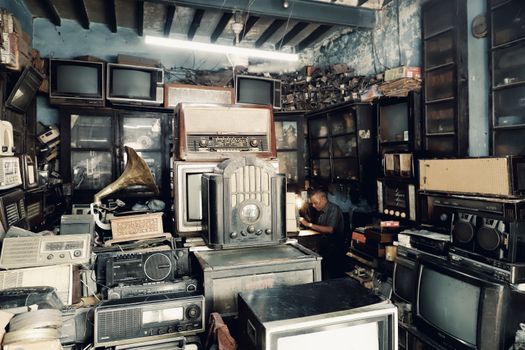 A cluttered vintage shop filled with antique radios, TVs, and a man working in the background.