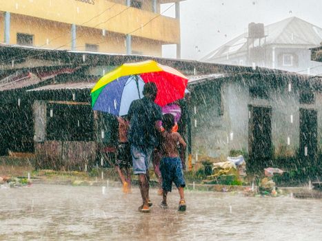 A man and child share a rainbow umbrella in the rain, creating a vivid street scene.
