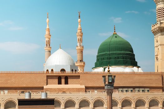 Beautiful view of the Prophet's Mosque in Madinah featuring its iconic green dome and minarets under a clear sky.