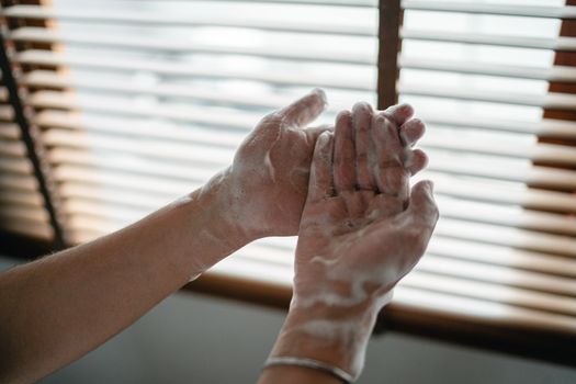 Close-up of adult hands covered in soapy foam against a window light backdrop.