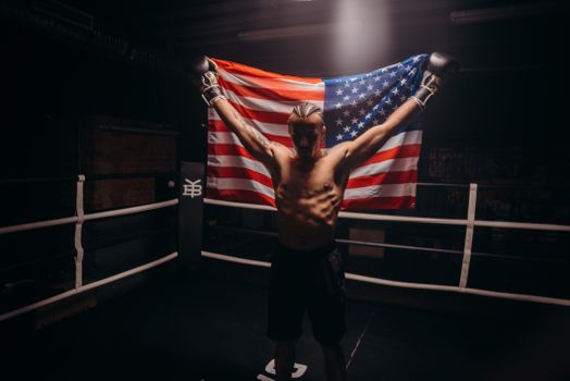 Shirtless boxer triumphs in the ring while holding an American flag, symbolizing victory.