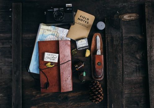 Overhead of vintage photo camera near leather notebook with map and camera roll near knife and cone placed on table