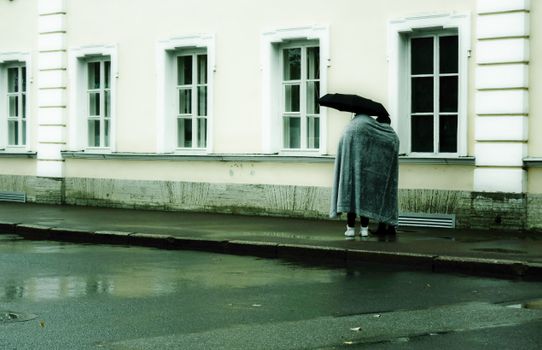 Couple under a blanket sharing an umbrella on an urban sidewalk in rainy Saint Petersburg.