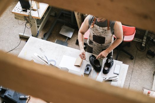 Top view of a leather artisan at work in a workshop, focusing on shoe crafting.