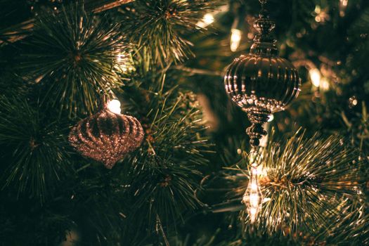 Close-up of sparkling Christmas ornaments hanging on a decorated tree with warm lights.