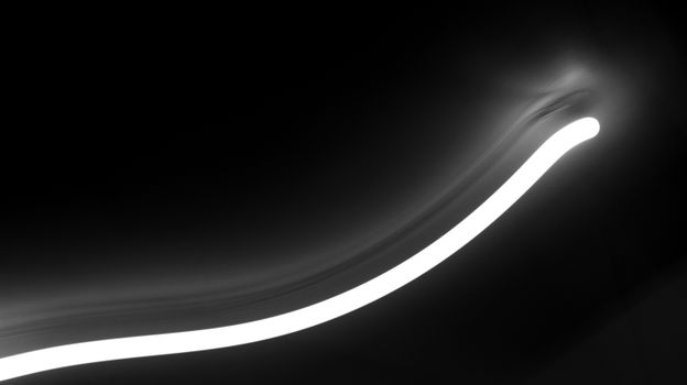 Black and white of abstract luminous curved neon line on black background in long exposure